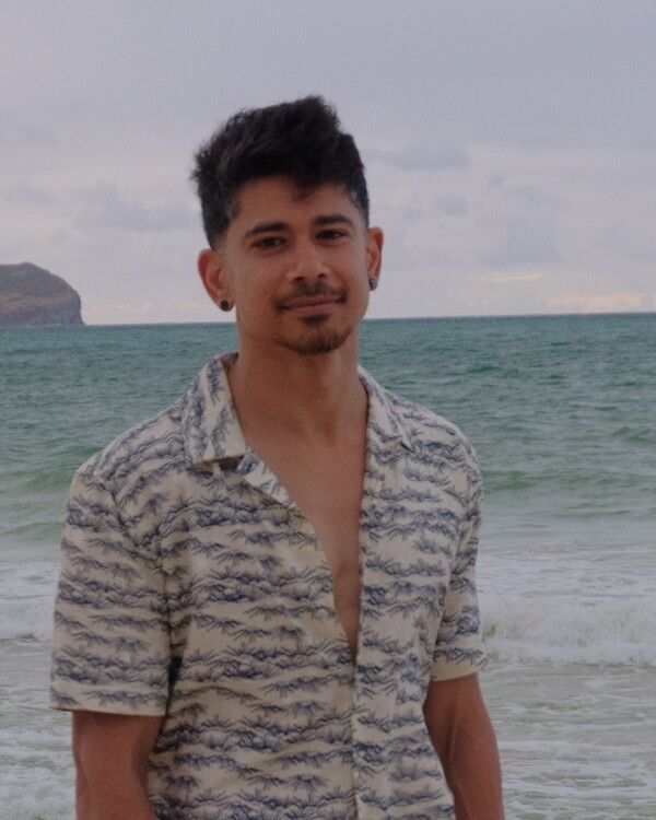 Sundar on a beach, ocean and headland behind him